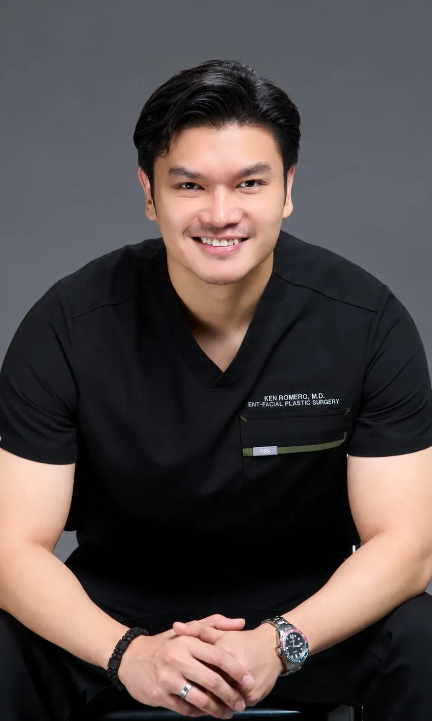 Dr. Ken Romero in black surgical scrubs, smiling